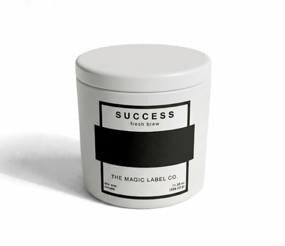 Success Candle from the magic label co. in a white container with lid and the label is inactive hiding the message 